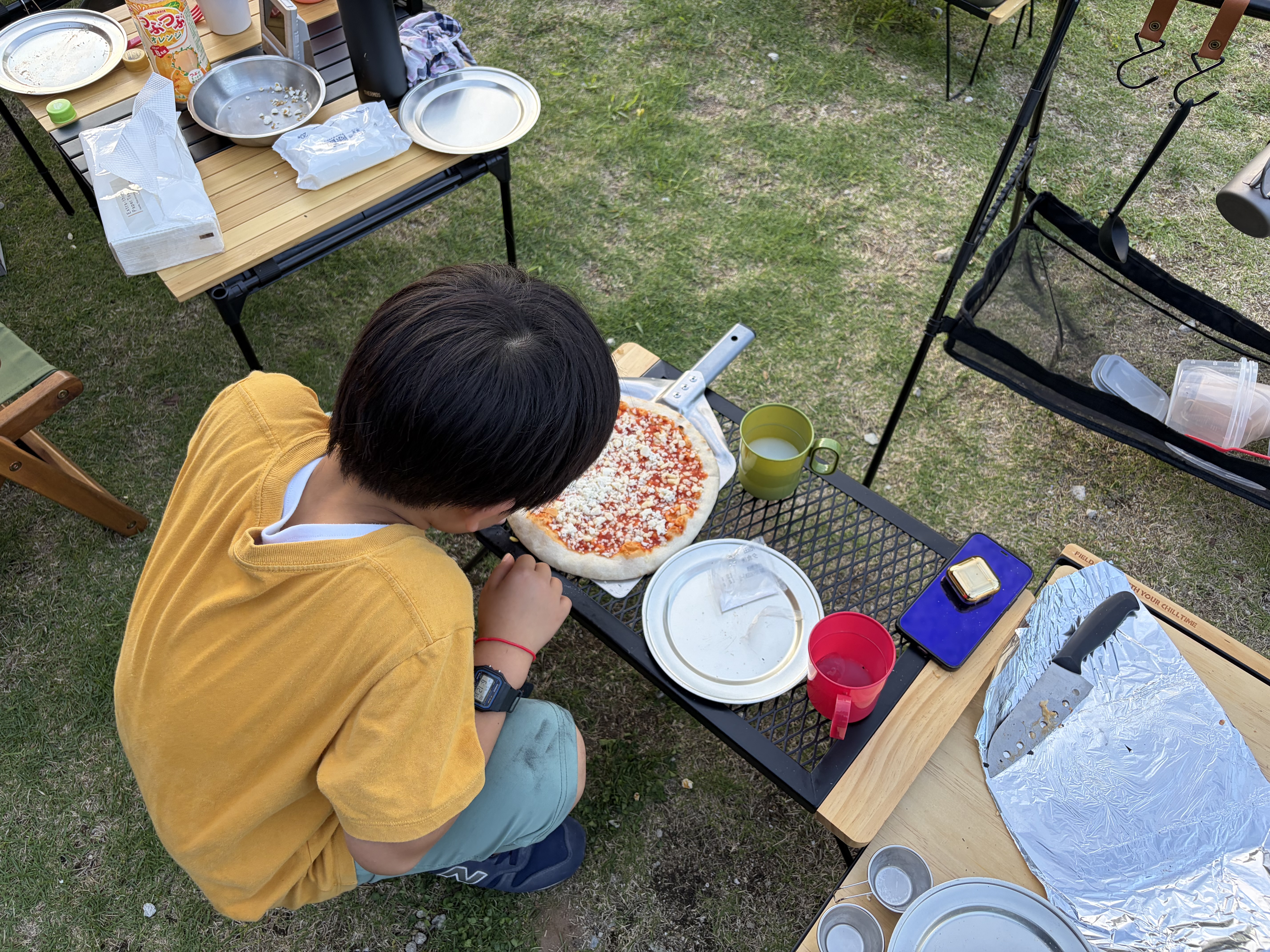 子どもがキャンプで冷凍ピザにトッピングしている様子